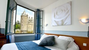 A bedroom with a large window, a bed with white and gray bedding, a blue blanket, and a white rose painting on the wall. - Logis Hotel du Chateau (Josselin)