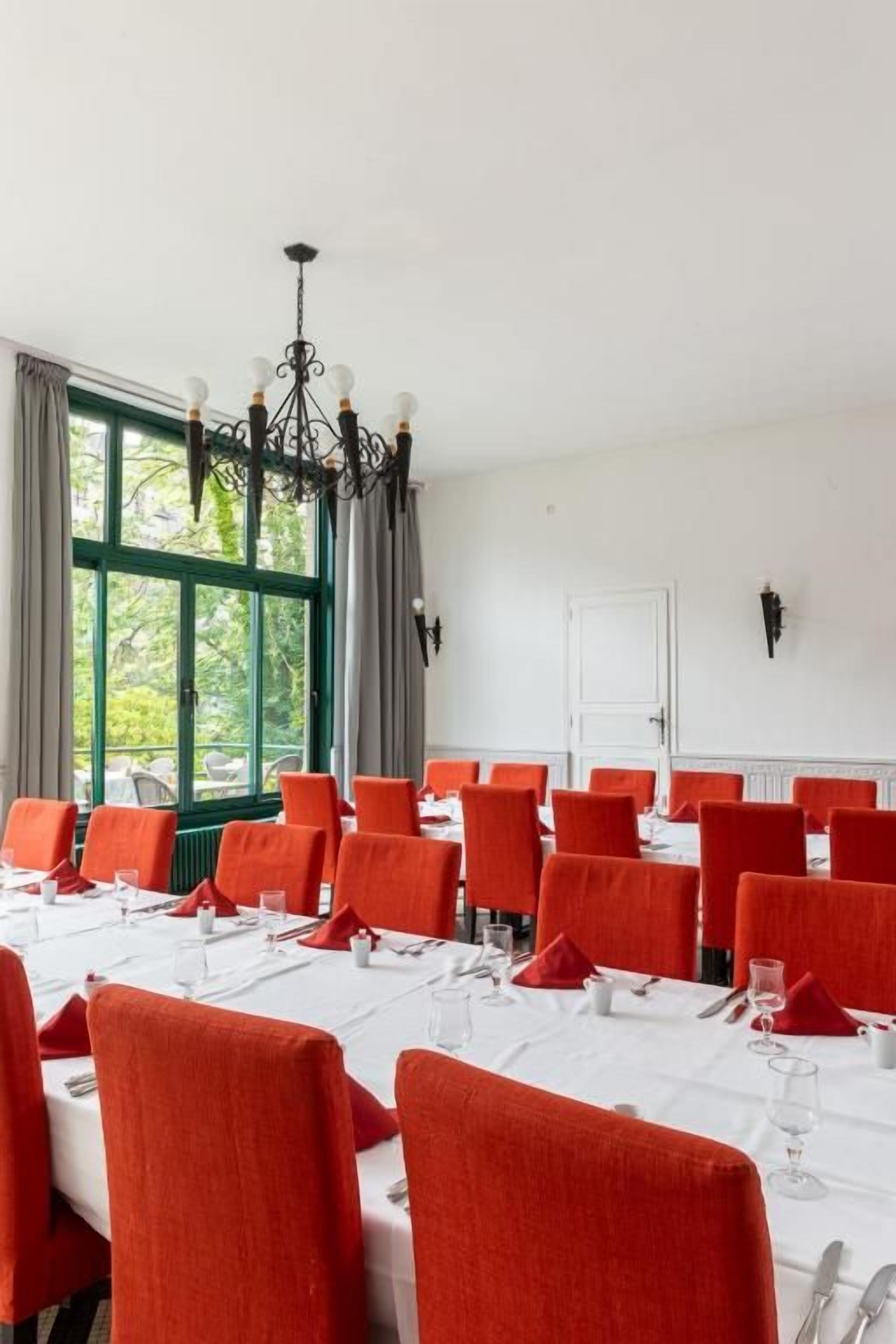 Une salle de conférence avec des tables dressées pour un repas, un lustre et une vue par la fenêtre.