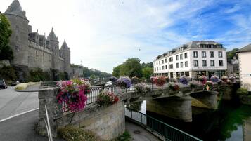 Un château historique en pierre, doté de nombreuses tours, un pont agrémenté de jardinières et un bâtiment moderne avec une enseigne indiquant la présence d’un restaurant.