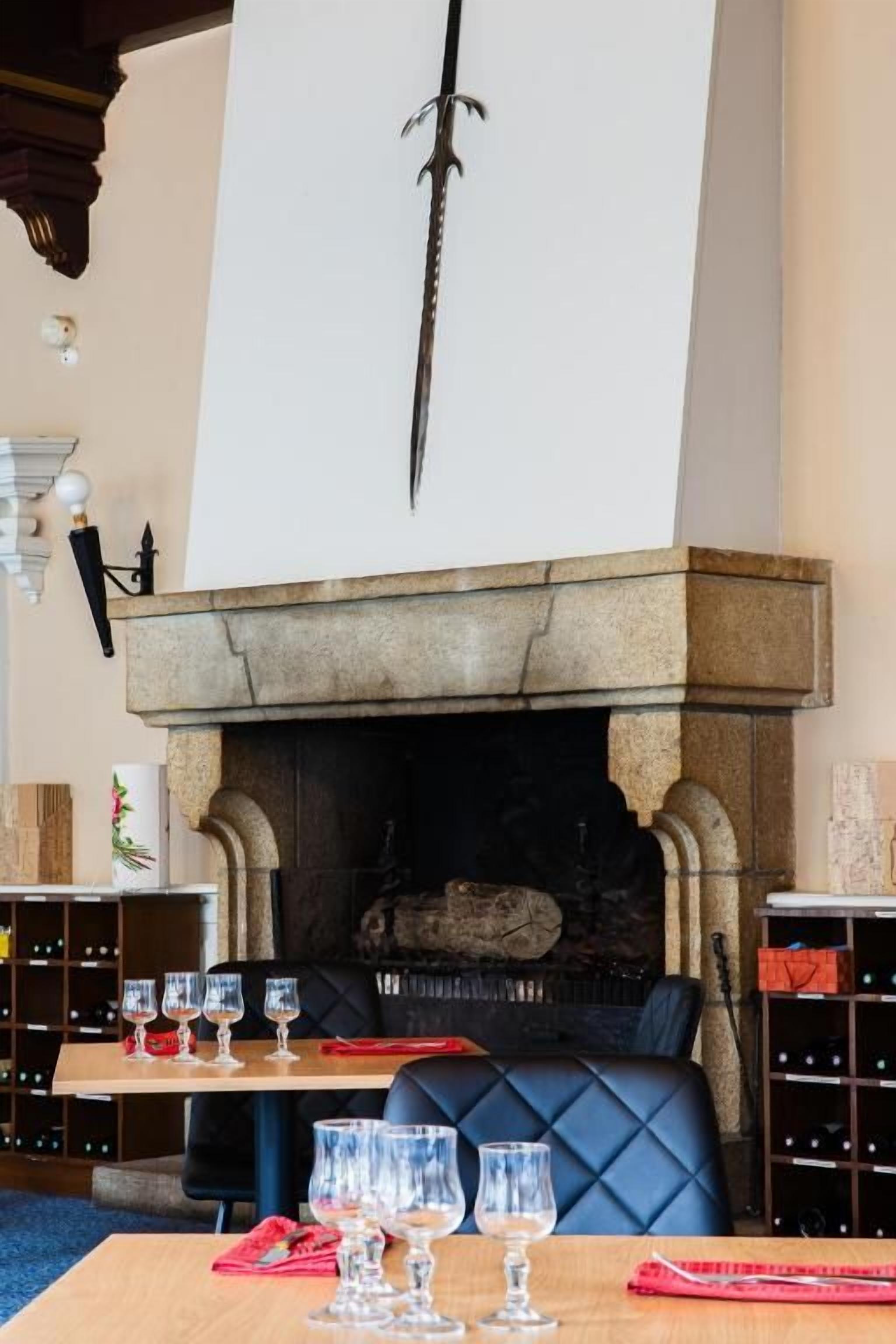 A dining area with a stone fireplace, a sword mounted above it, and a table set with wine glasses.