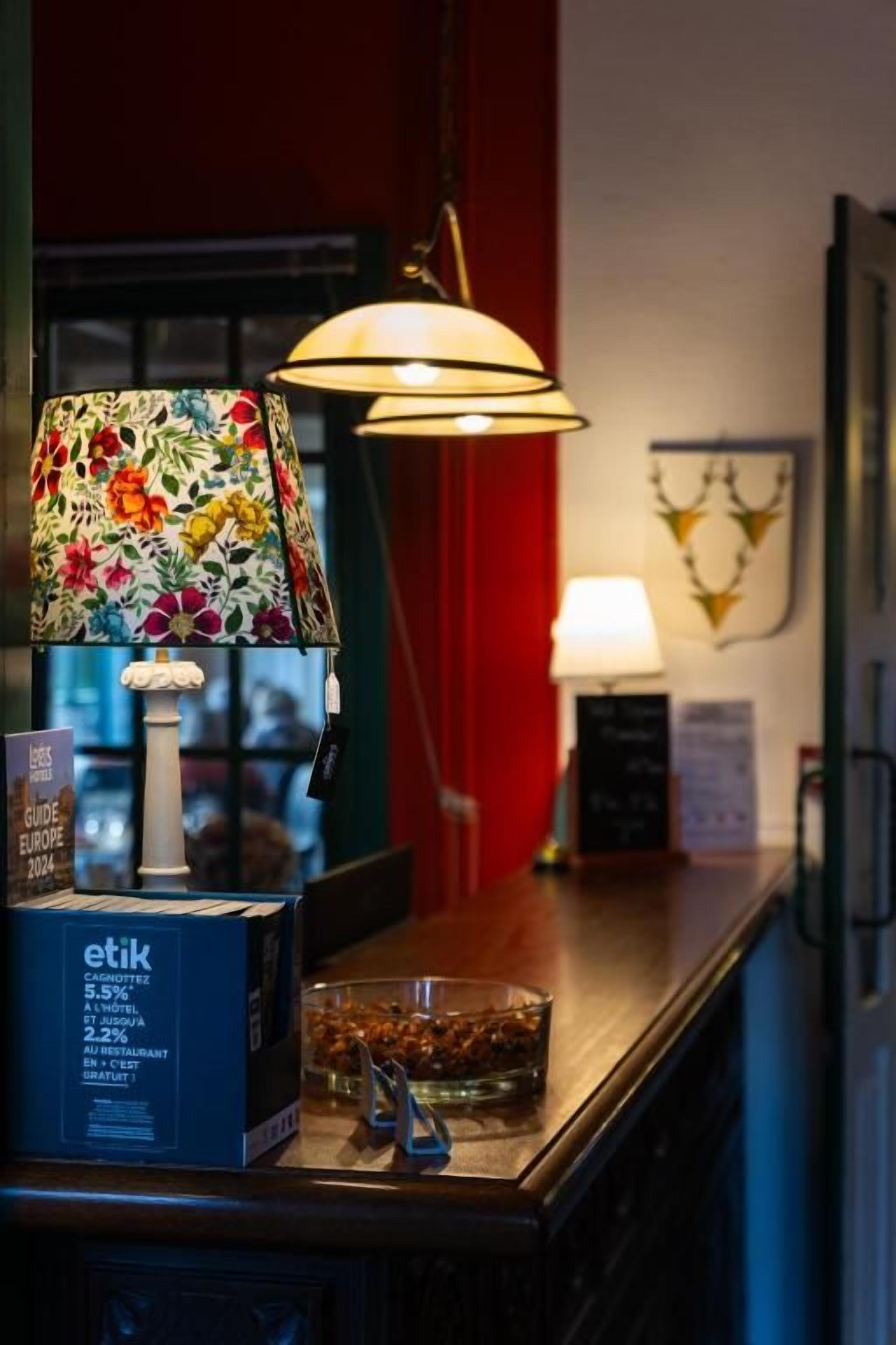 Ett bord med en ask Etik-kaffe, en blommig lampa och en ljusstake.