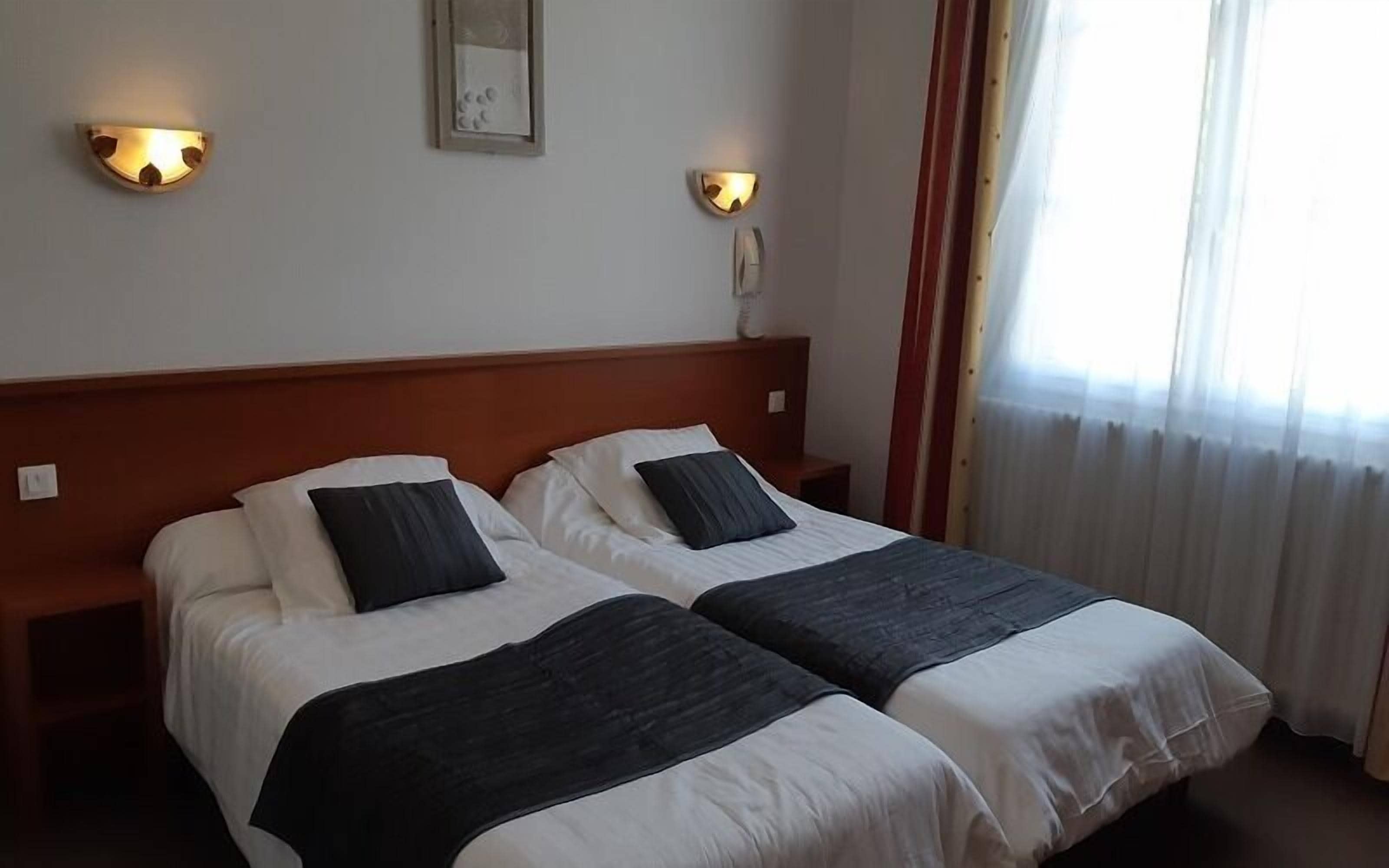 A double room with two beds, each with white linens and dark headboards. There are wall-mounted light fixtures on either side of a mirror.