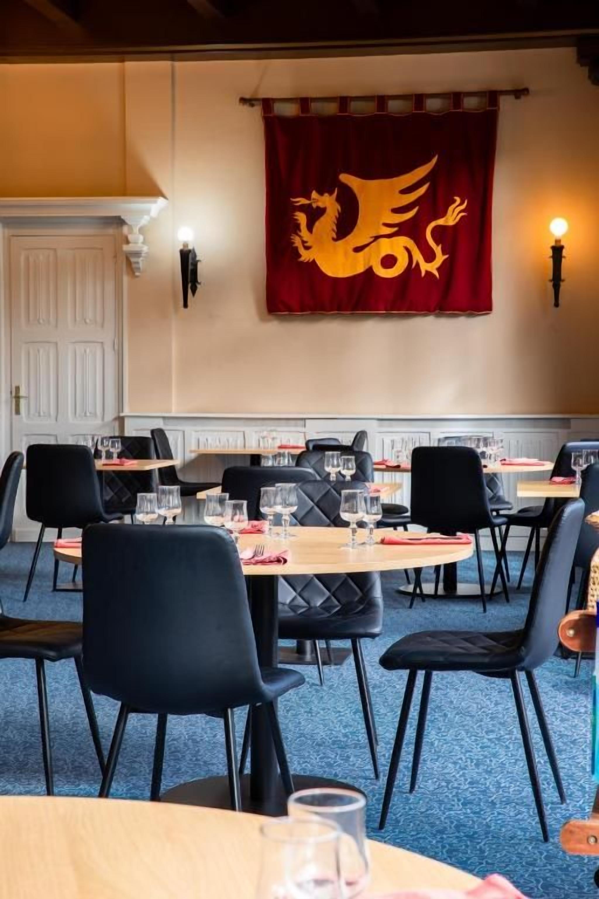 Un comedor con mesas y sillas, una cortina roja con un diseño de dragón y luces fijadas a la pared.