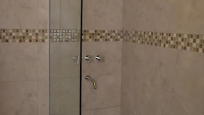 A glass-enclosed shower stall with a bathtub.