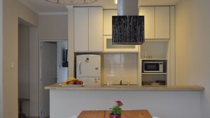 A modern kitchen with white cabinets, a microwave, and a refrigerator. There is a wooden table with a potted plant in the foreground.