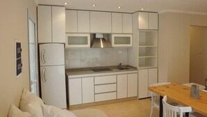 A compact kitchen with white cabinets, a built-in microwave, and a sink. There is a dining table with chairs and a small refrigerator.