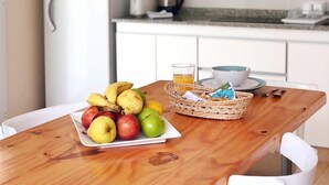 A kitchen with white cabinets, a wooden table with fruits, a basket, and a kettle.