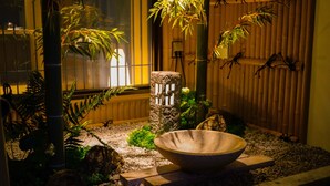 A serene indoor garden with a stone basin, bamboo plants, and a wooden fence.