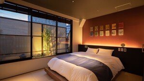 A modern bedroom with a large bed, a view of the outside through a sliding door, and a wall with framed artwork.