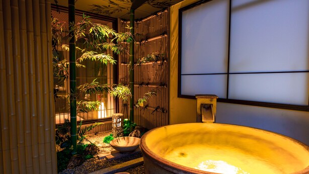 A traditional Japanese room with tatami flooring, a large wooden bathtub, and bamboo plants.