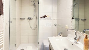 Een moderne badkamer met een douchecabine van glas, een witte wastafel met spiegel en een toilet.