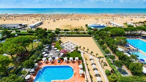 A resort with a large pool area, multiple sun loungers, and a beach in the background. - Hotel Italy (San Michele al Tagliamento)