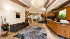 A hotel lobby with a reception desk, seating area, chandelier, and decorative elements. - Hotel Italy (San Michele al Tagliamento)