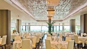 A large banquet hall with round tables, chairs, and a central chandelier. - Hotel Italy (San Michele al Tagliamento)