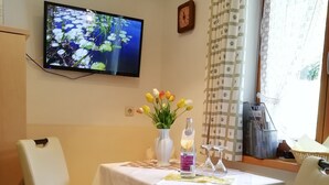 En matplats med ett bord dukat för två personer, en tv som är monterad på väggen och ett fönster med gardiner.