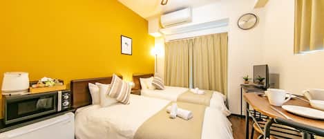 A hotel room with two beds, a microwave, a small refrigerator, a dining table with chairs, and a clock on the wall.