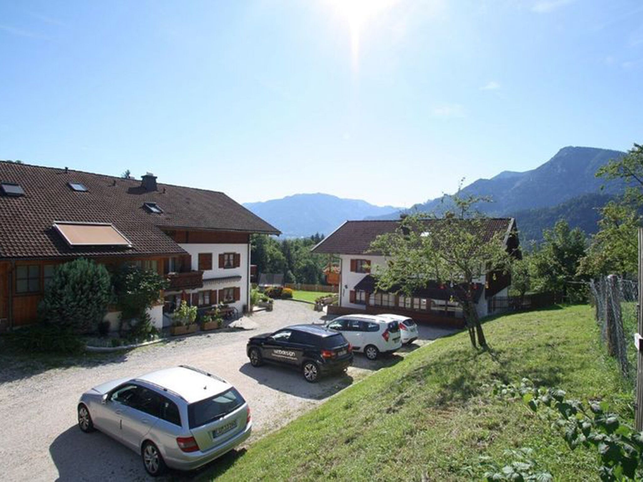 Ein Wohngebiet mit Häusern, einem Schotterweg, parkenden Autos und einer Bergkulisse im Hintergrund.
