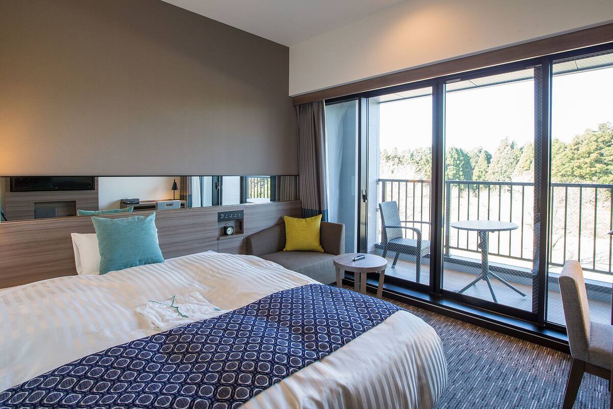 A modern hotel room with a large bed, a TV, a small table, and a balcony with a chair.