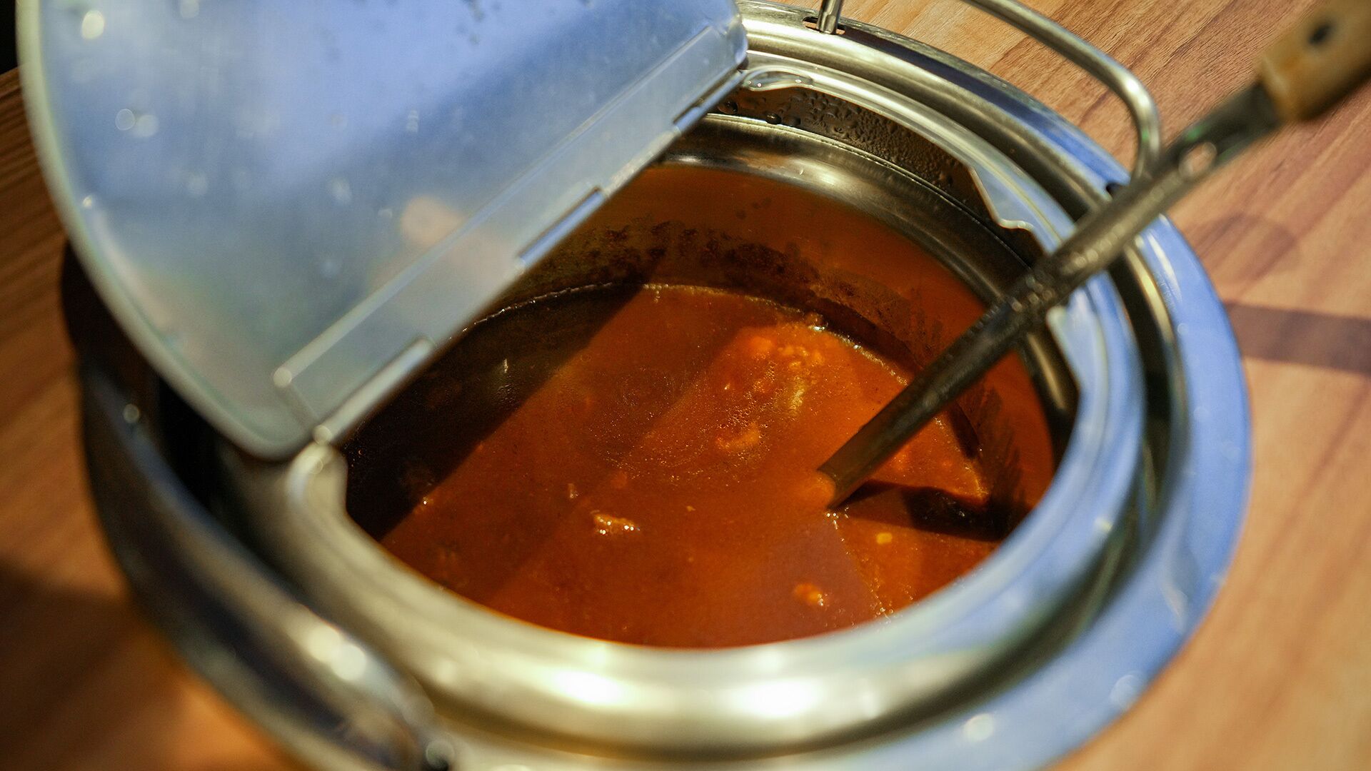 A metal container with a lid, possibly a soup or stew, on a wooden surface.