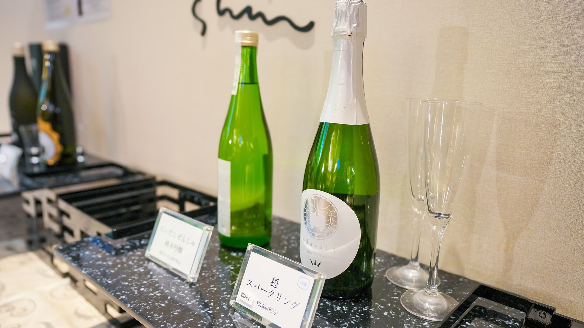 Disposición para una cata de vinos con dos botellas verdes y una copa sobre una encimera, mostrando etiquetas y precios.