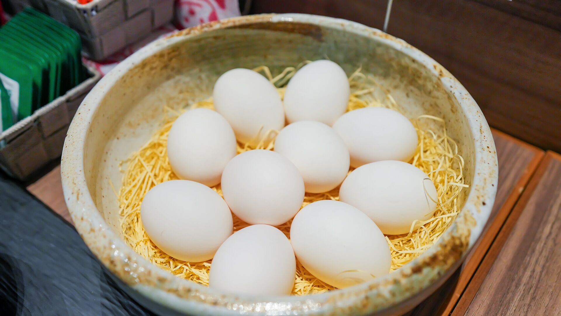 A ceramic bowl containing eggs and straw on a wooden surface.