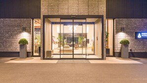 A hotel entrance with a glass door, potted plants, and a sign for the AIA HOTEL KUMAMOTO. - Airport Hotel Kumamoto (Ozu)