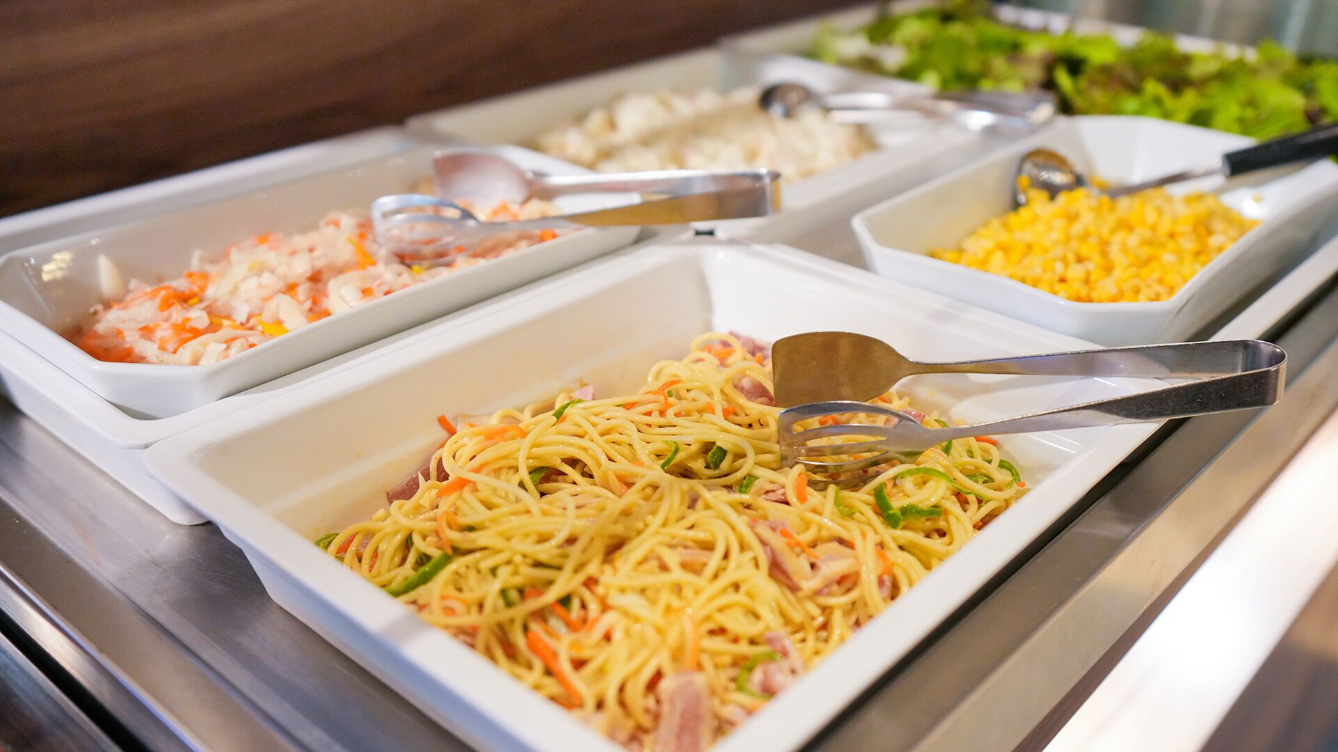Un bufé con diversos platos, incluyendo pasta, camarones y maíz.