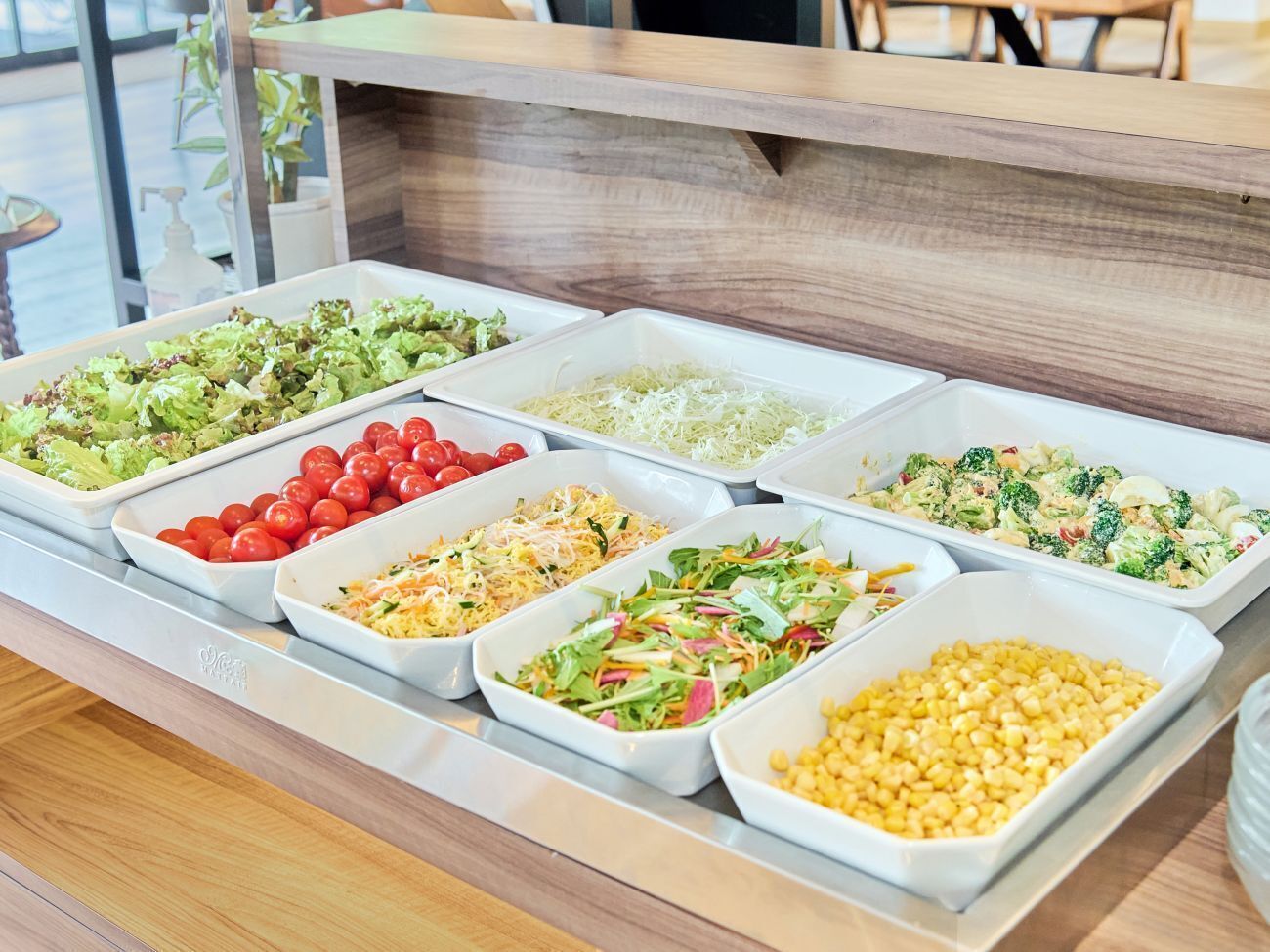 Un bufé con diversas opciones de comida, entre ellas ensaladas, verduras y cereales.
