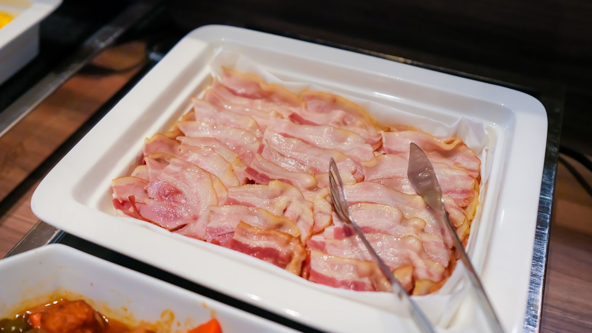 Un plat rectangulaire blanc contenant des tranches de jambon et un couteau.