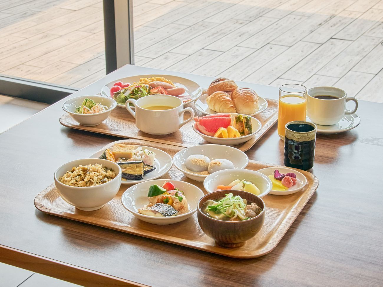 Bandeja de desayuno con diversos platos y bebidas sobre una mesa de madera cerca de una ventana.