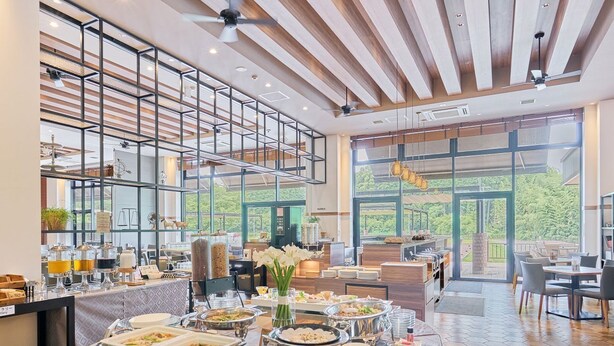 A buffet setup with various food stations, a large window offering a view of greenery, and a ceiling fan. - Airport Hotel Kumamoto (Ozu)