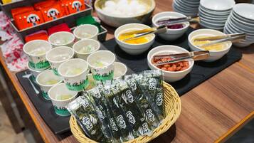 A table with various food items, including cups of tea, bowls of food, and a basket of seaweed snacks.