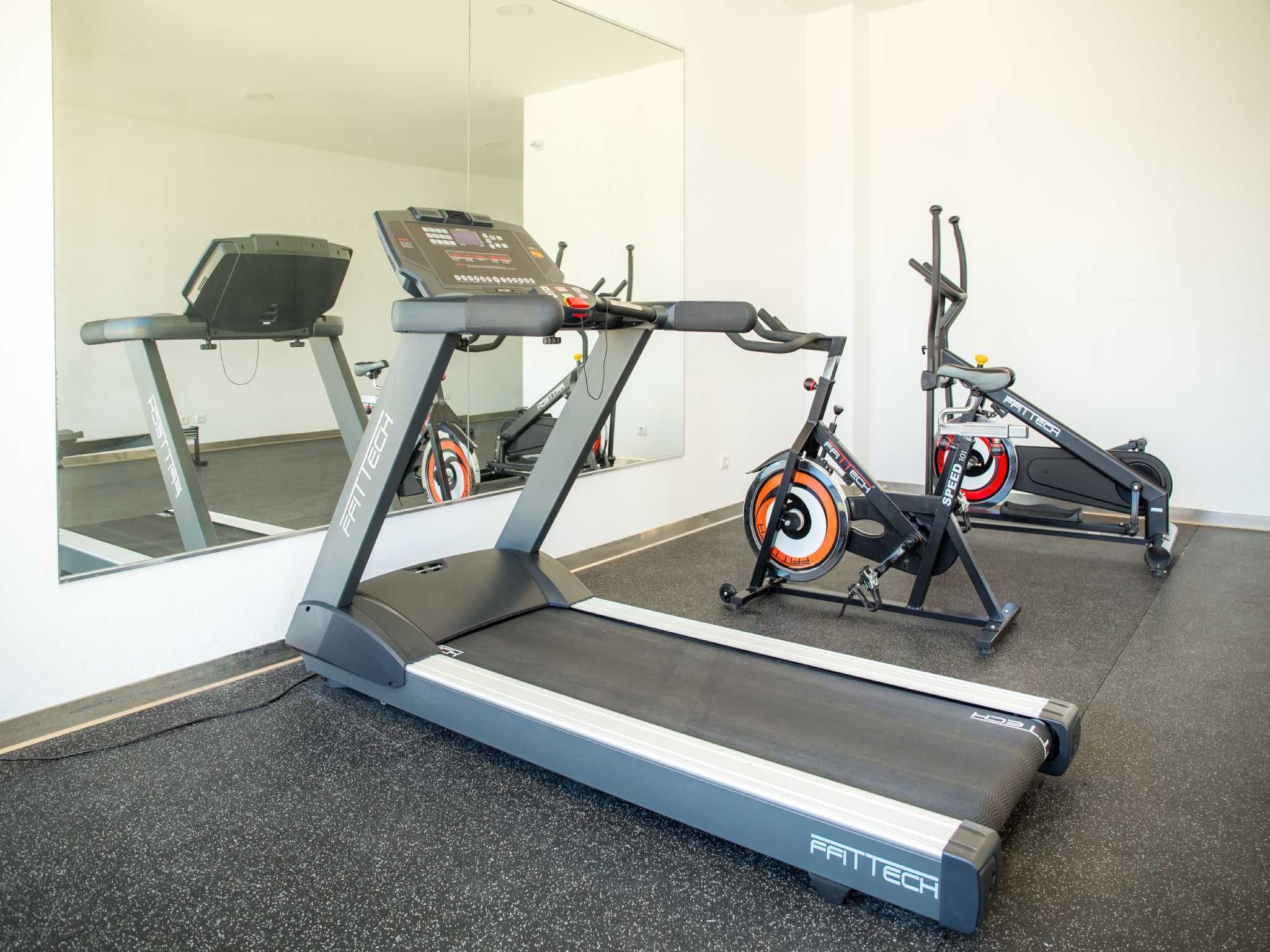 Un gimnasio con cintas de correr y bicicletas estáticas, un espejo y un suelo negro con motas.