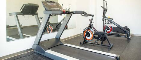 Un gimnasio con cintas de correr y bicicletas estáticas, un espejo y un suelo negro con motas.