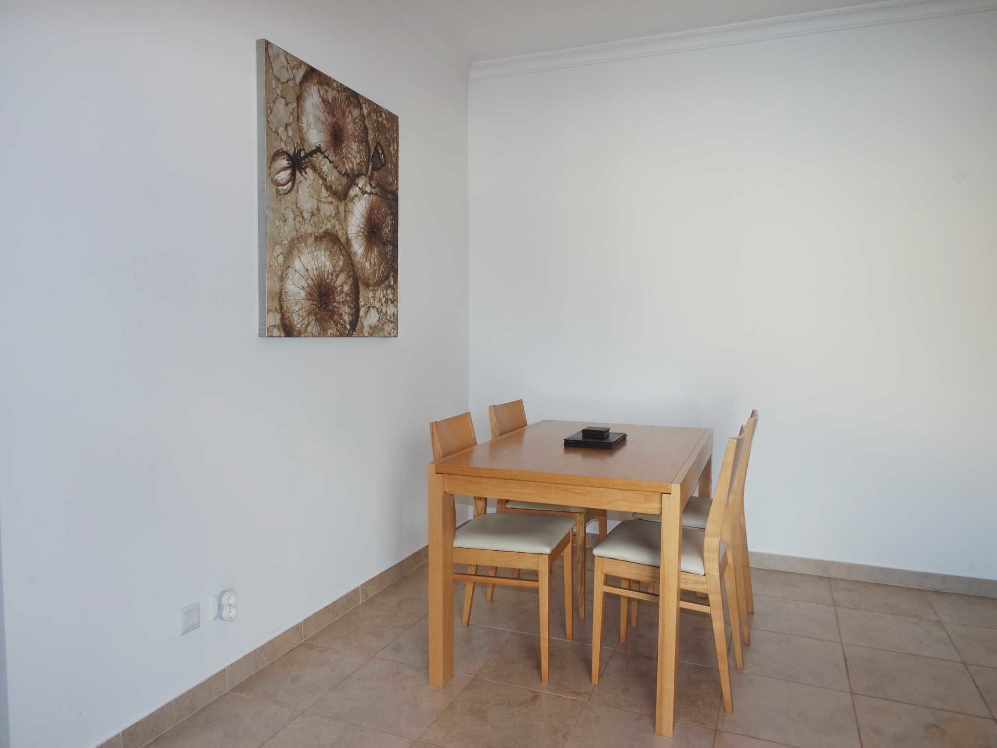 A dining area with a wooden table and chairs, a painting on the wall, and a tiled floor.