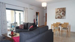 Una sala de estar moderna con un sofá gris, una mesa de comedor con sillas y un ventanal con cortinas.