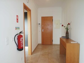 Un pasillo con un extintor, una puerta de madera y un florero con flores sobre una encimera de madera.
