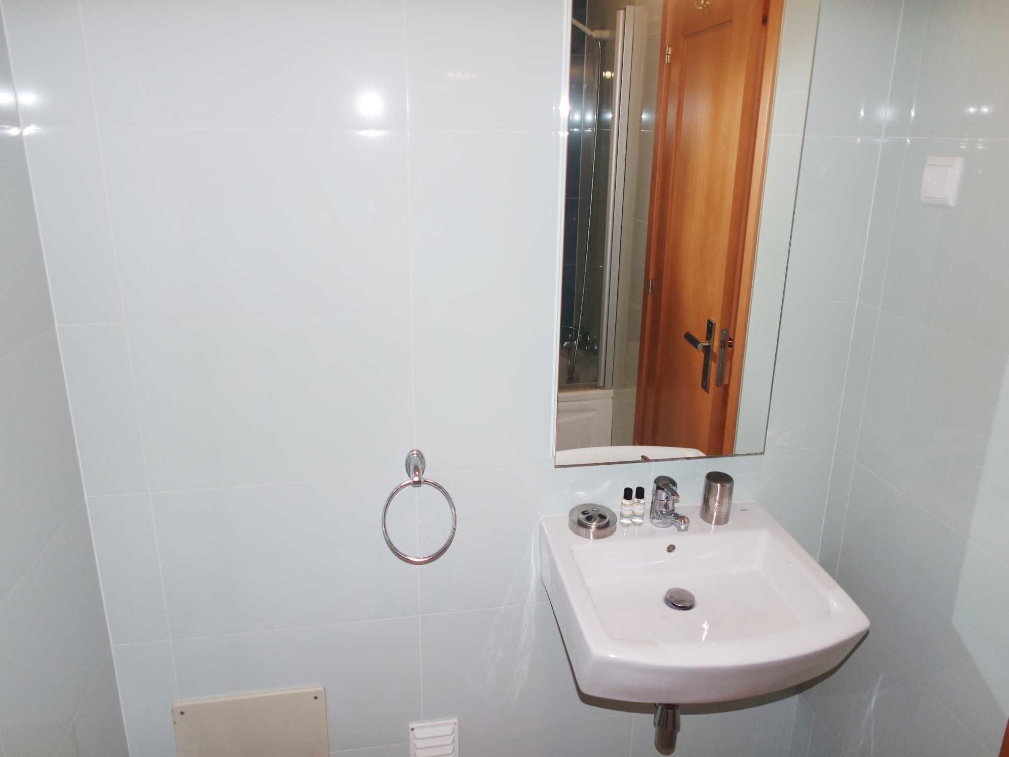 Un bagno con un lavandino bianco, uno specchio e un porta asciugamani.