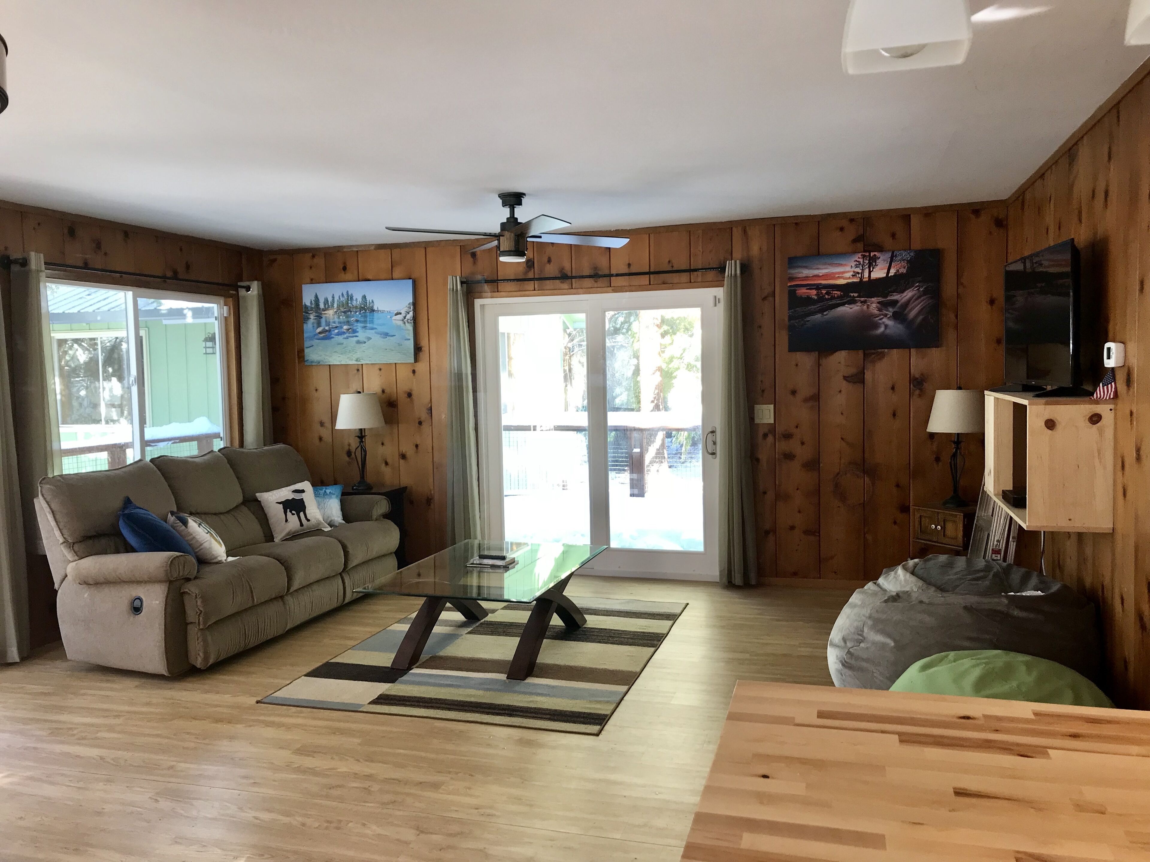 A cozy living room with a sofa, a glass coffee table, a wooden TV stand, and a ceiling fan.