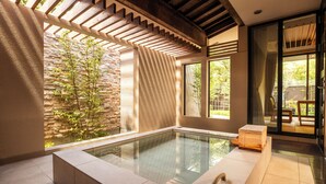 A modern indoor pool area with a stone wall, wooden beams, and large windows.