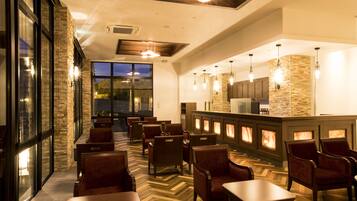 A restaurant with a herringbone floor pattern, wooden tables and chairs, and a stone accent wall.