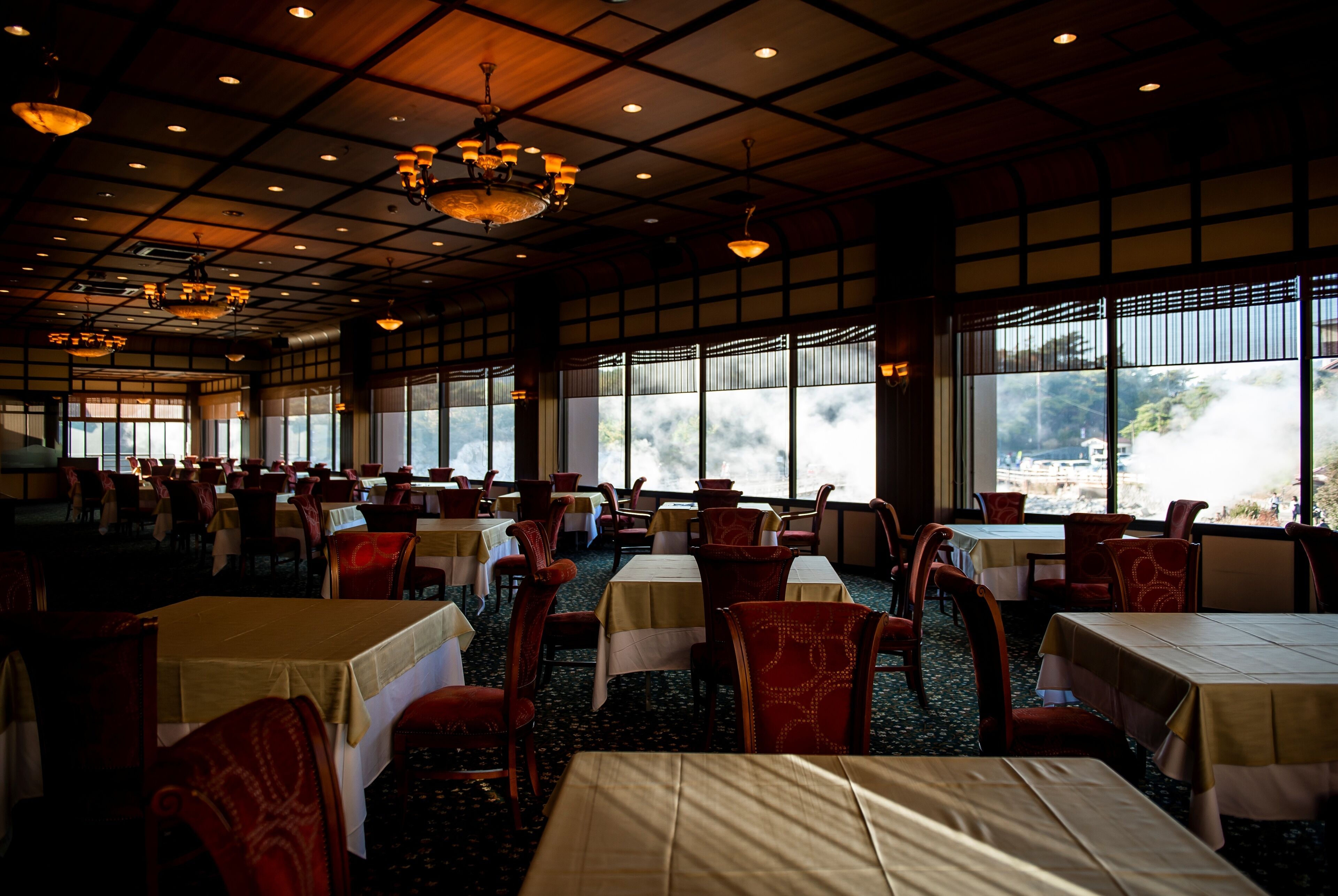 A spacious dining area with tables and chairs, large windows, and a high ceiling with chandeliers.