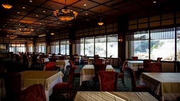 A spacious dining area with tables and chairs, large windows, and a high ceiling with chandeliers.