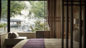 A hotel room with a large window offering a view of a forested area and a building emitting steam.
