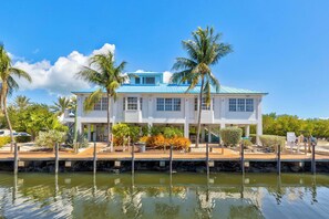 A waterfront property with a blue-roofed building, palm trees, and a dock. - Deja Blue Oceanfront Condo- 2 Lanais, Pool + Beach (Tavernier)