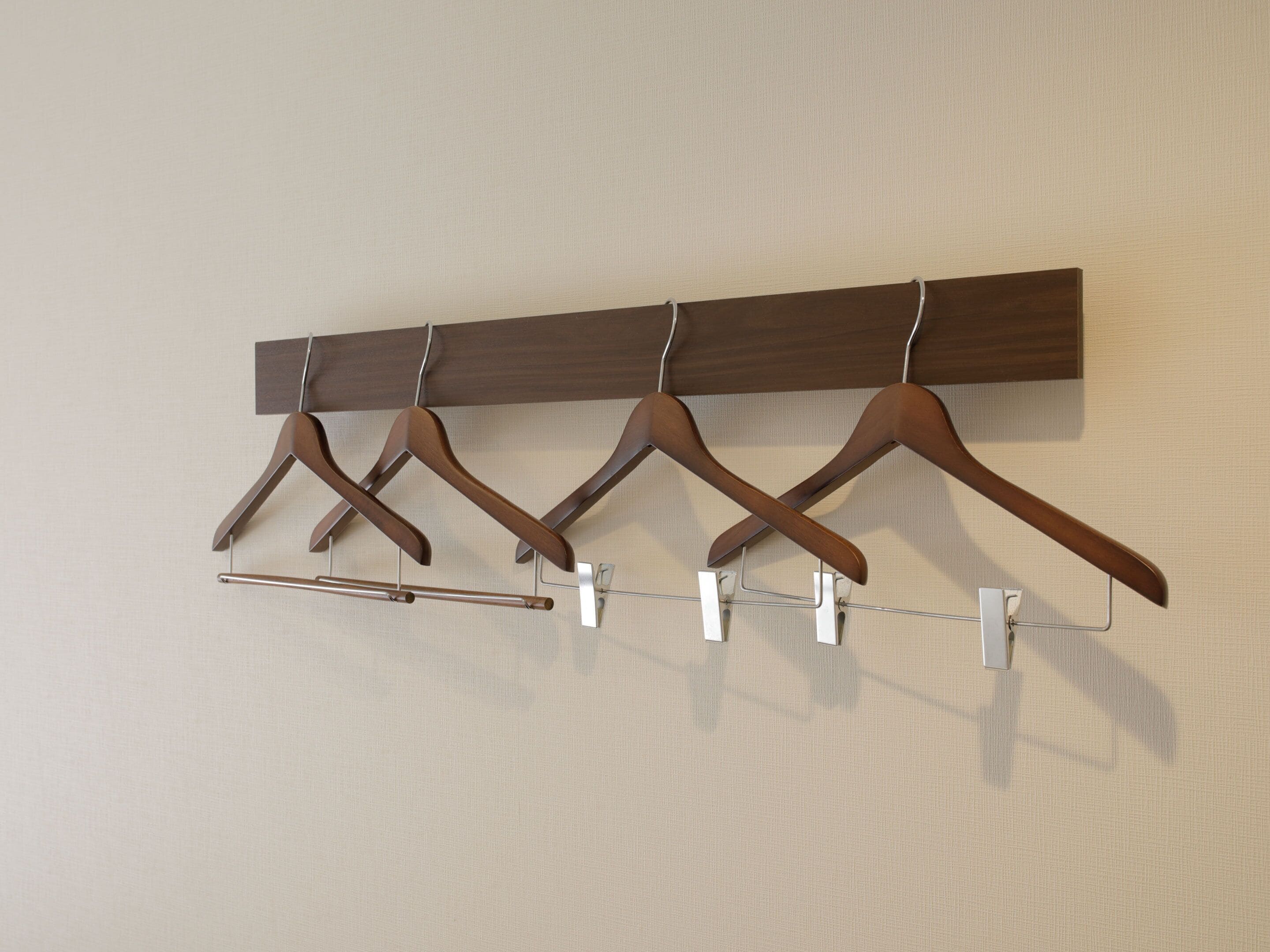 A wall-mounted wooden coat rack with four wooden hangers and a metal hanger bar.