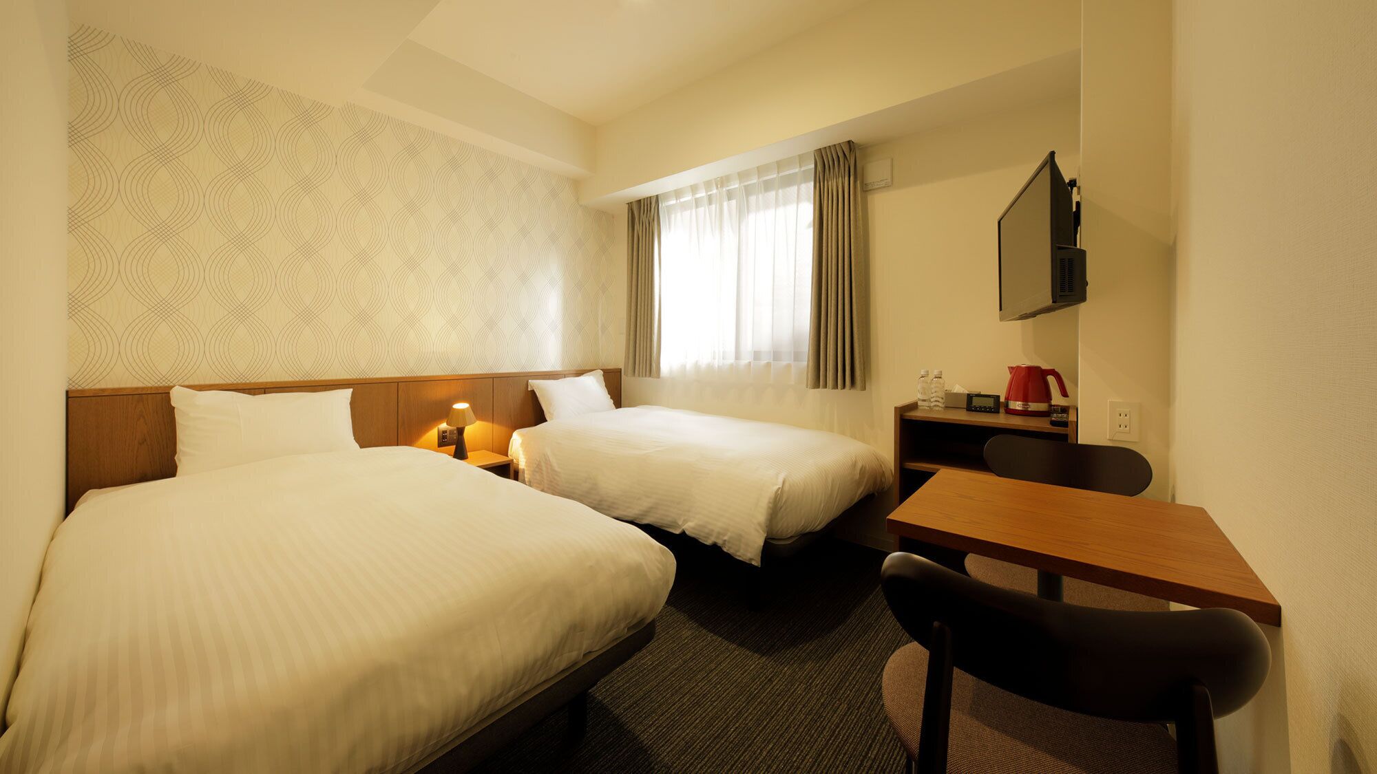 Ett hotellrum med två sängar, ett skrivbord, en stol, en TV och ett fönster med gardiner.