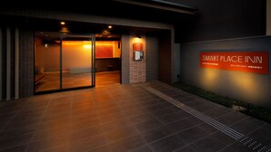 Esterno di un hotel dal design moderno, con ingresso in vetro, una targa con il nome dell'hotel e un vialetto lastricato che conduce all'ingresso.