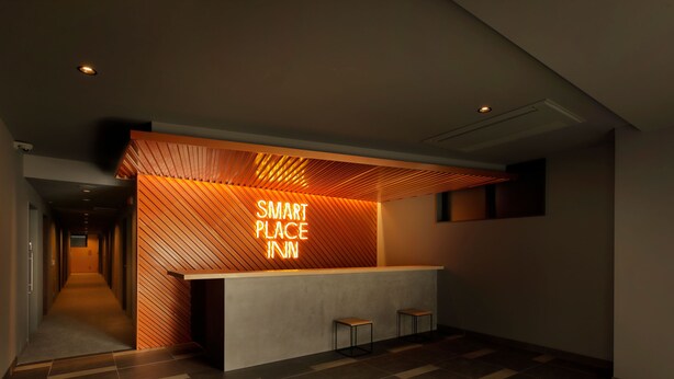 Un'area reception moderna con un'insegna 'Smart Place Inn', un soffitto in listelli di legno e un pavimento piastrellato.
