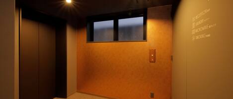 A hotel room with a carpeted floor, a window with a view, and a wall with a reception sign.
